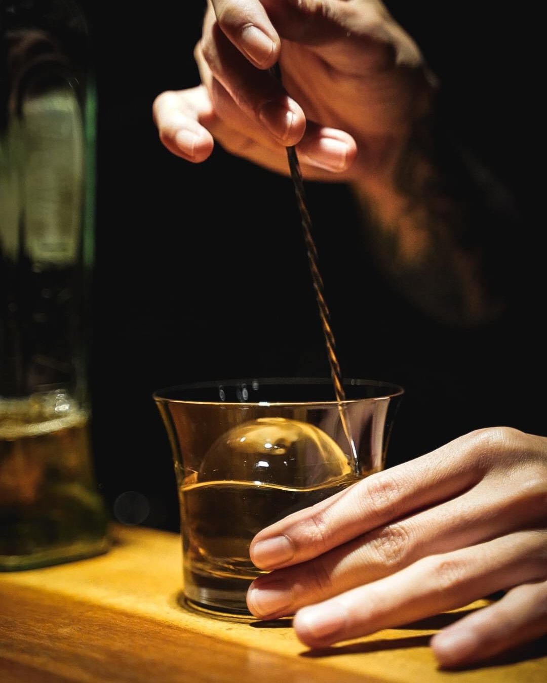 A bartender working with a bar spoon and a short glass