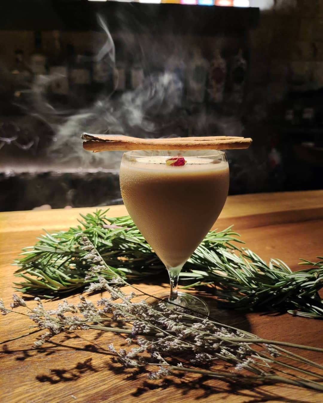 A stemmed glass framed by herbs and rising smoke